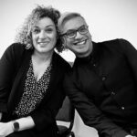 A woman and a man lean on to each other whilst smiling