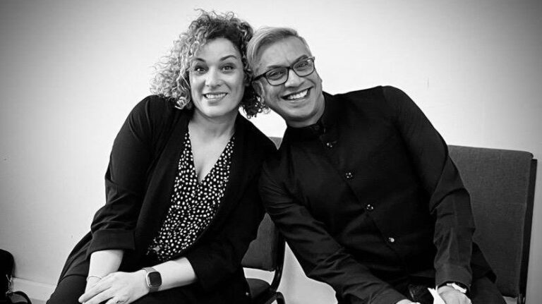 A woman and a man lean on to each other whilst smiling