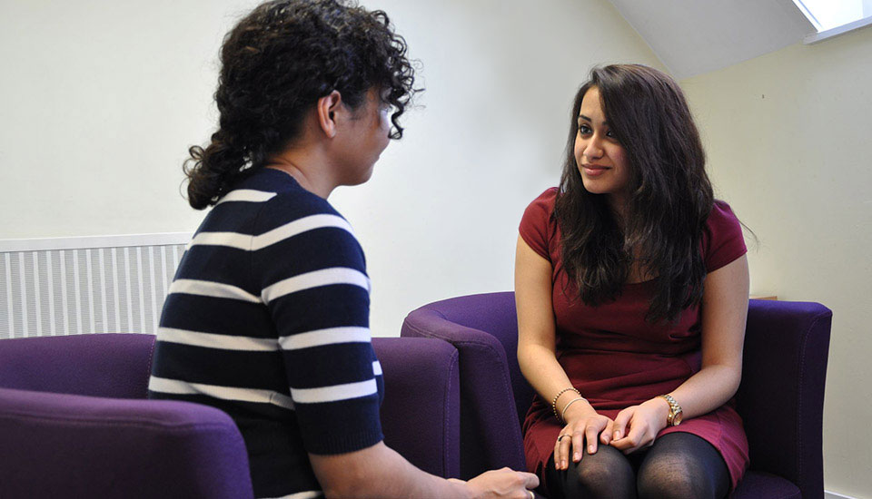 Two women sitting facing each other, one looks at the other with kindness