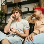 Two friends share a serious moment during a phone call on a cozy couch.