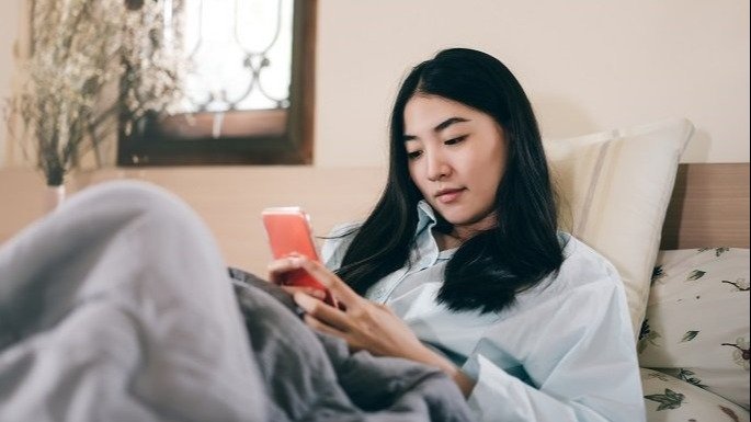 Women looks at her phone whilst lying in bed