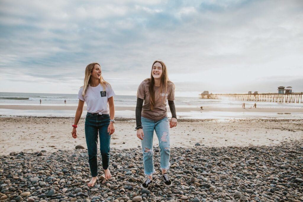 Two young women smiling as they walk on a beach
