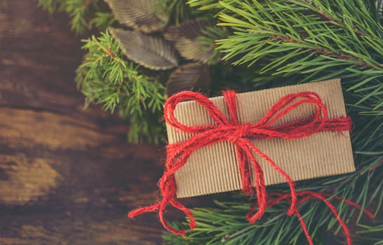 A beautifully wrapped Christmas gift box tied with a red bow sits on fresh pine branches.