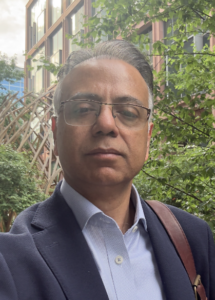 Man with glassess looking at the camera with trees in the background